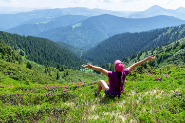 
Girl in a pink hat raising her hands to the sky in a flowering green-pink mountain valley in the Ukrainian Carpathians
