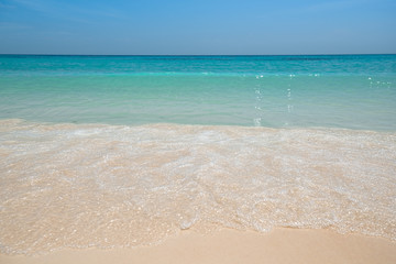 Tropical sea with beautiful aquamarine water and white foam wave breaking on fine yellow sand beach. Seascape Background. Thailand