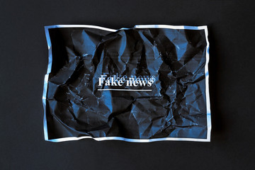 Paper sheet with Fake news inscription. Crumpled sheet of dark paper