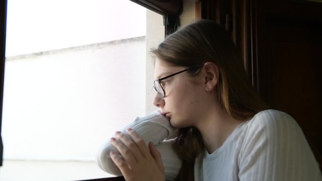 Sad unhappy millenial girl looking on Window, bored Thoughtful sadness on teenager Face, Isolated People Quarantined at Home, Virus Epidemic Outbreak