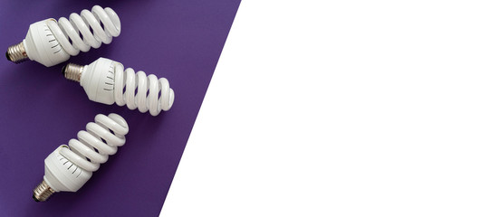 Closeup of white halogen spiral fluorescent light bulb on violet and white background, saving energy and eco concept, top view, banner, space for text.