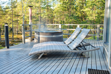 Traditional Finnish wooden hot tub and two chaise longues on a terrace with forest background.