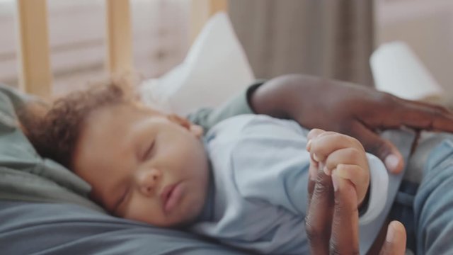 Close up of mixed-race sweet kid sleeping on his father. African male hands patting sleeping infant