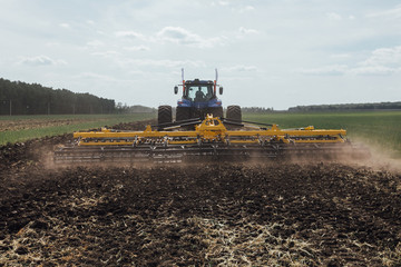 Fototapeta premium blue tractor in the field harrowing the land with a plow while driving