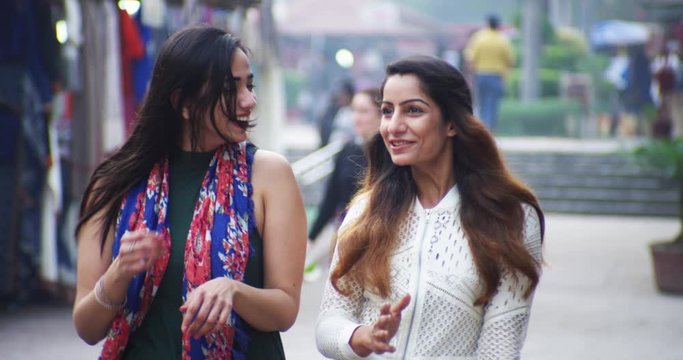 4K Happy Indian female friends walking through street market, chatting & laughing. Slow motion.