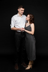Studio portrait of an affectionate loving husband kissing his wife with eyes closed and smiling in her forehead. Couple snuggling close on black background. Love concept.