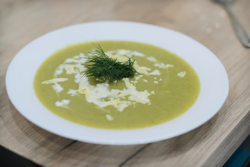Broccoli soup with dill and sour cream in a white plate on the wooden background.