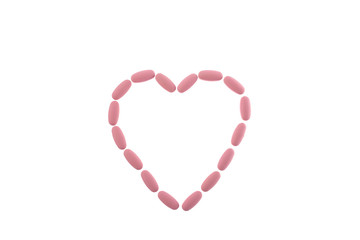 Pink pills in the shape of a heart on a white isolated background. Daily Vitamins dose. Heart shape made of tablets for therapy, concept of treatment and health care. Copy space.