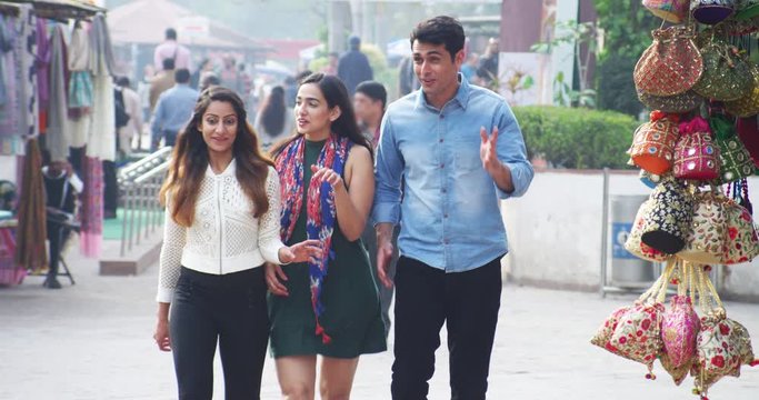 4K Happy Indian friends walking through busy city market, chatting & laughing