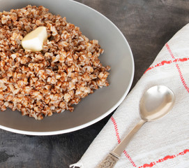 boiled buckwheat with butter in a gray plate and spoon and napkin on a dark background