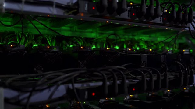 Large wired internet datacenter storage. Cryptocurrency mining equipment on large farm. ASIC miners on stand racks mine bitcoin in server room. Supercomputer blinking with lights. Light effects.