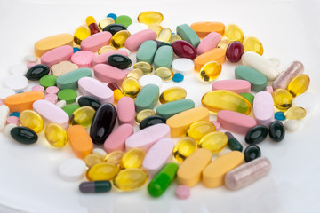 A pile of pills on a white plate symbolizing food. Vitamins on a white isolated background. Pink pills and burgundy softgels. Prescription meal replacement for everyday meals. open aperture.