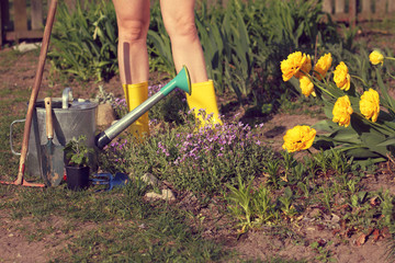 gardener with bare feet in yellow boots next to a flower bed and garden tools. decorate your site for the summer