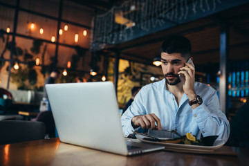 man using laptop and talking on mobile phone while having lunch in restaurant