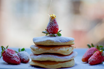 Stack of delicious fluffy pancakes with fresh strawberries and sugar and honey