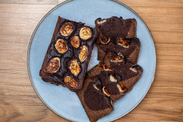 Homemade banana bread cut into slices on a blue plate. Cutted banana on top. Easy to prepare and healthy, home made pastry.