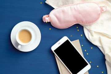 Sleeping app for insomnia, fall asleep concept. Flat lay home desk with cup of coffee, sleep mask, blanket and smartphone with blank screen mockup
