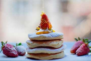 Stack of delicious fluffy pancakes with fresh strawberries and sugar and honey