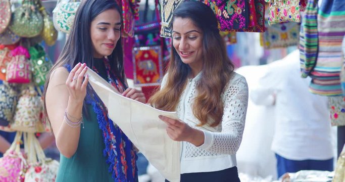 4K Smiling Indian girls shopping for textiles in busy city market. Slow motion.