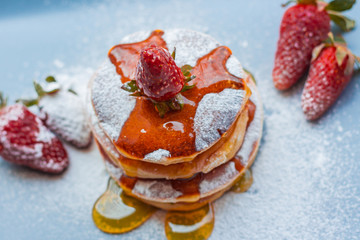 Stack of delicious fluffy pancakes with fresh strawberries and sugar and honey