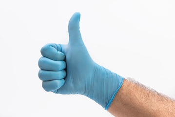 Hand with medical blue latex protective gloves showing thumbs up on white background held up as positive 

sign and resistance to pandemic