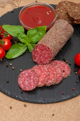 sliced smoked sausage with sauce, cherry tomatoes and basil on a black graphite board with slices of bread. top view