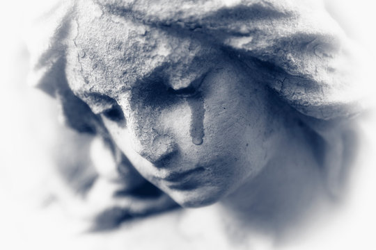 Death concept. Close Up of ancient stone statue of crying angel with tears in face as symbol of end of human life. Black and white image.