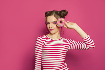 Happy woman holding donut on colorful pink background, diet concept