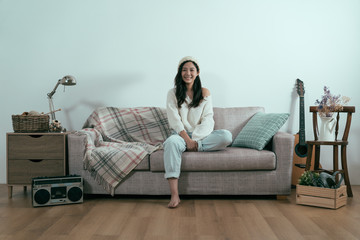 Obraz premium beautiful asian korean woman in sweater relax sitting on sofa face camera smiling with white blank background. charming girl in winter morning in living room at home. Lifestyle happy peaceful concept