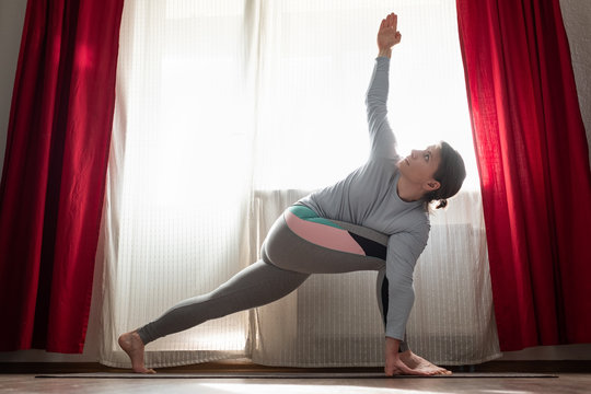 Sporty Attractive Young Beginning Yoga Woman Doing Lunge Exercise For Spine, Utthita Parsvakonasana In The Living Room.