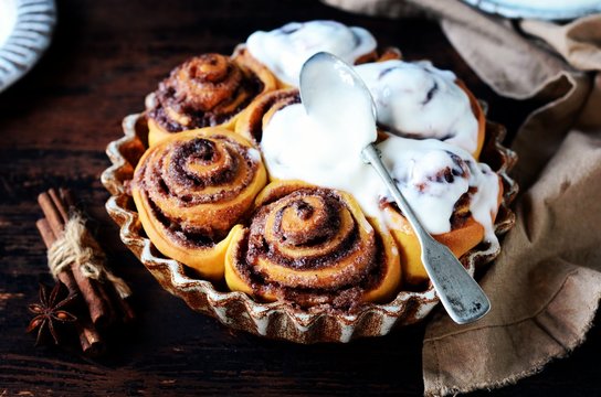 Cinnamon Rolls Baked in Ceramic Mold with Cream Cheese Icing on a Dark Wooden Background