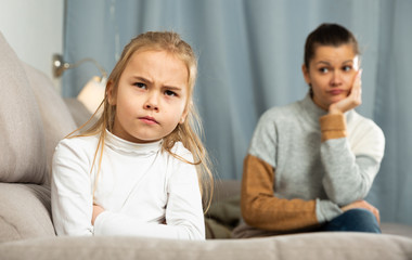 Frustrated small girl sitting at sofa,  having conflict with mother