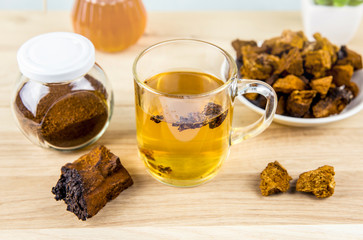 Wild natural chaga mushroom from birch tree, Inonotus obliquus pieces in tea glass on wooden table indoors home. Alternative traditional medicine.