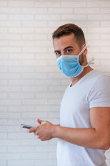 Man wearing an anti virus protection mask to prevent others from getting coronavirus COVID-19 and SARS cov 2, while communicating with loved ones with his smartphone from home.  