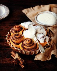 Cinnamon Rolls Baked in Ceramic Mold with Cream Cheese Icing on a Dark Wooden Background
