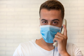 A man in a medical face protection mask to protect himself from the virus, inside his house, talking on the phone.