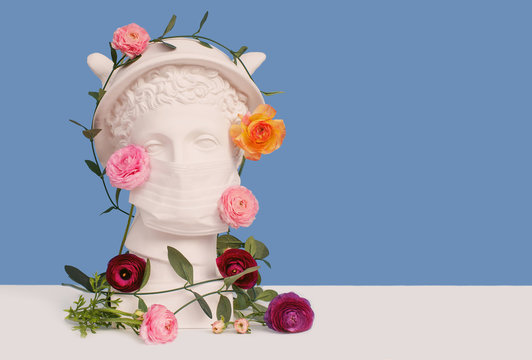 White plaster statue of a bust of god Mercurius in a disposable protective medical mask. Patron of trade and beneficiation. Coronavirus and covid-19 concept. Spring crisis. Space for text. Allergy