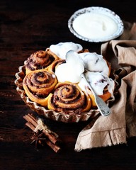Cinnamon Rolls Baked in Ceramic Mold with Cream Cheese Icing on a Dark Wooden Background
