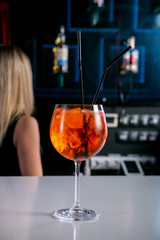 Aperol Cocktail. Fresh cocktail in a glass with ice on a white bar counter against a dark background. European lounge bar menu