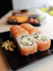 In the sushi bar in the kitchen on the table stands a sushi roll with salmon on a black plate