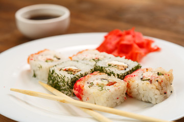 A set of rolls with dill and salmon on a plate with soy sauce, ginger and chopsticks.