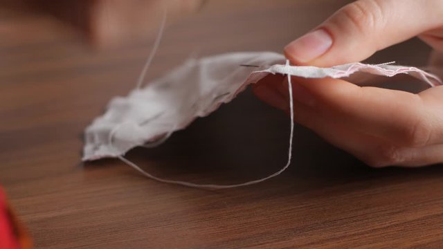 Hands of a young woman in a sewing thimble from white cotton fabric at night in the house. Making your own reusable protection masks. Extreme close-up view of a woman's hands.