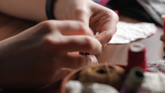 Hands of a young woman in a sewing thimble from white cotton fabric at night in the house. Making your own reusable protection masks. Close-up view of a woman's hands.
