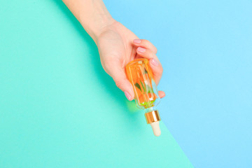  Beautiful young woman's hands with  oil bottle  on pastel background .