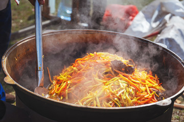 Cooking pilaf in a large cauldron outside on a picnic. Cooking Uzbek holiday pilaf. Carrots and...