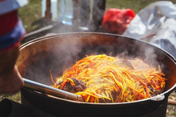 Cooking pilaf in a large cauldron outside on a picnic. Cooking Uzbek holiday pilaf. Carrots and...