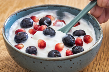 Bowl of yogurt, fresh blueberries, and seeds of pomegranate . Healthy breakfast, close up