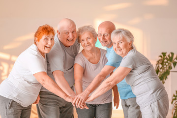 Happy elderly people putting hands together in gym