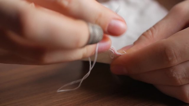 Hands of a young woman in a sewing thimble from white cotton fabric at night in the house. Making your own reusable protection masks. Extreme close-up view of a woman's hands.