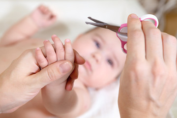 Close up view at fingernails cutting, mother with small scissors and her baby hand